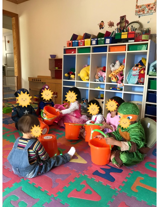 Children playing together on the alphabet mat beside toy shelves; their faces have stickers