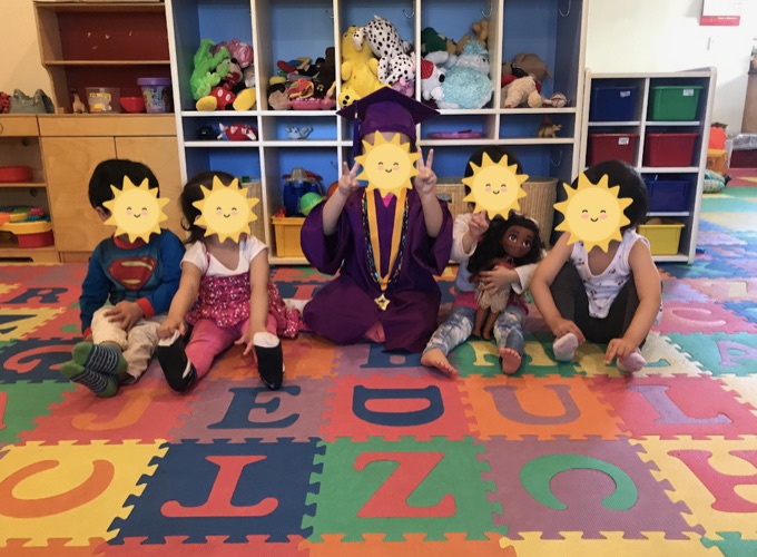 A group of children sitting together on the colorful playroom mat; their faces have stickers