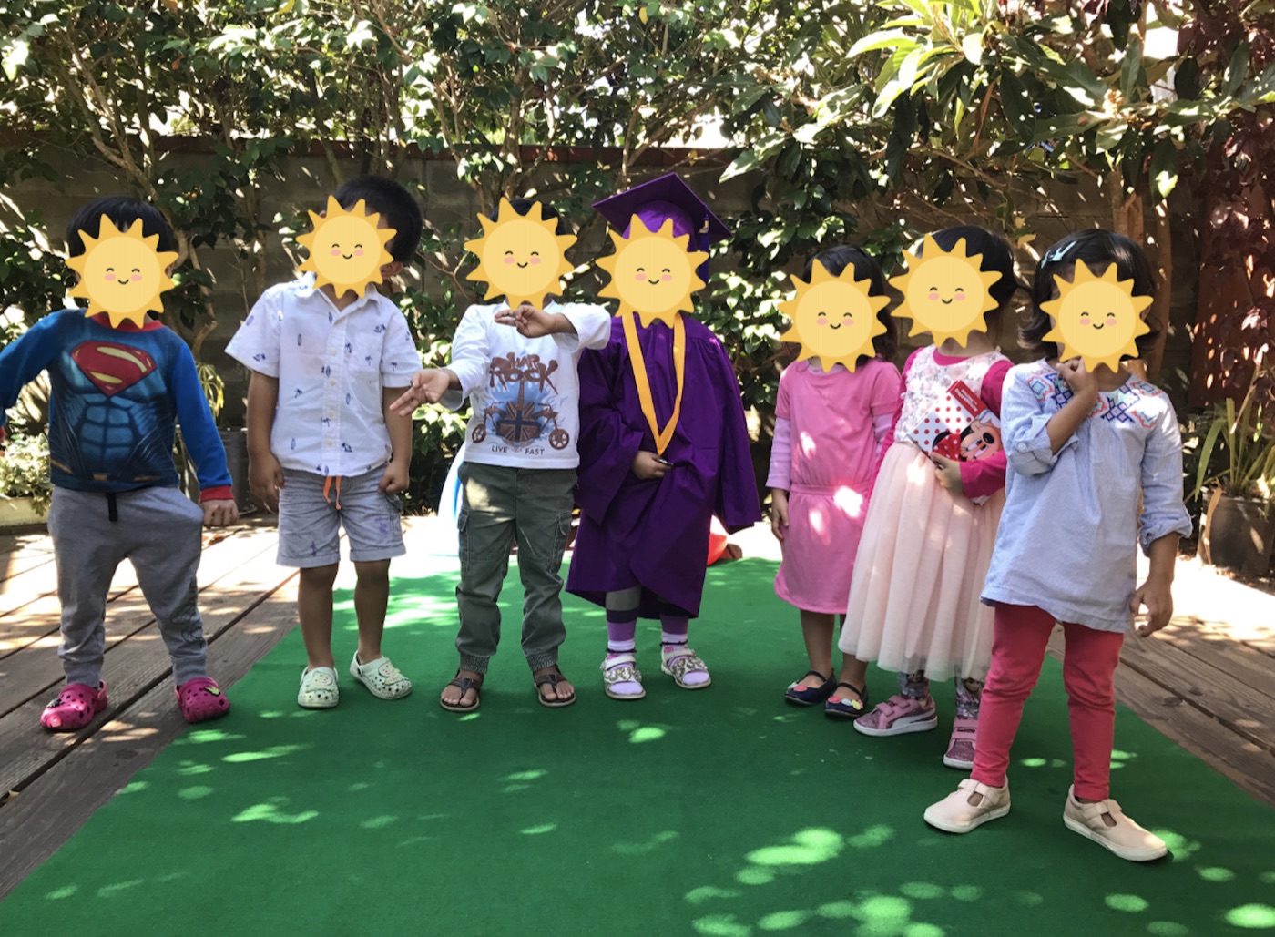 Children with face-covering stickers standing together in Little Star’s shaded backyard